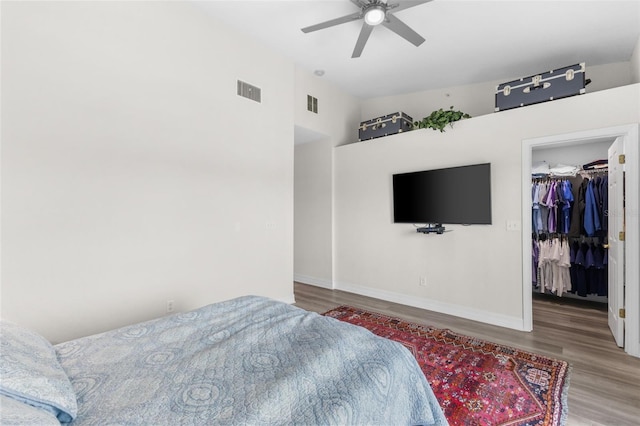 bedroom with wood finished floors, a walk in closet, baseboards, and a ceiling fan