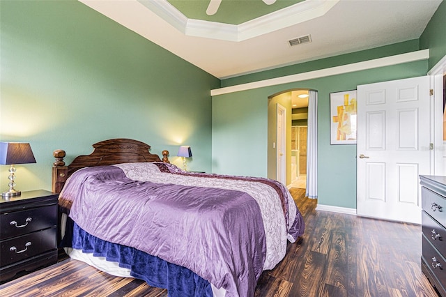 bedroom with dark wood-type flooring, a raised ceiling, ceiling fan, and ornamental molding