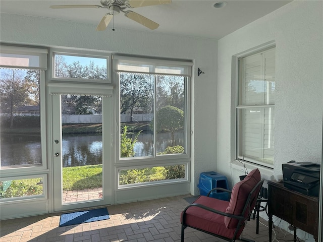 sunroom featuring ceiling fan and a water view