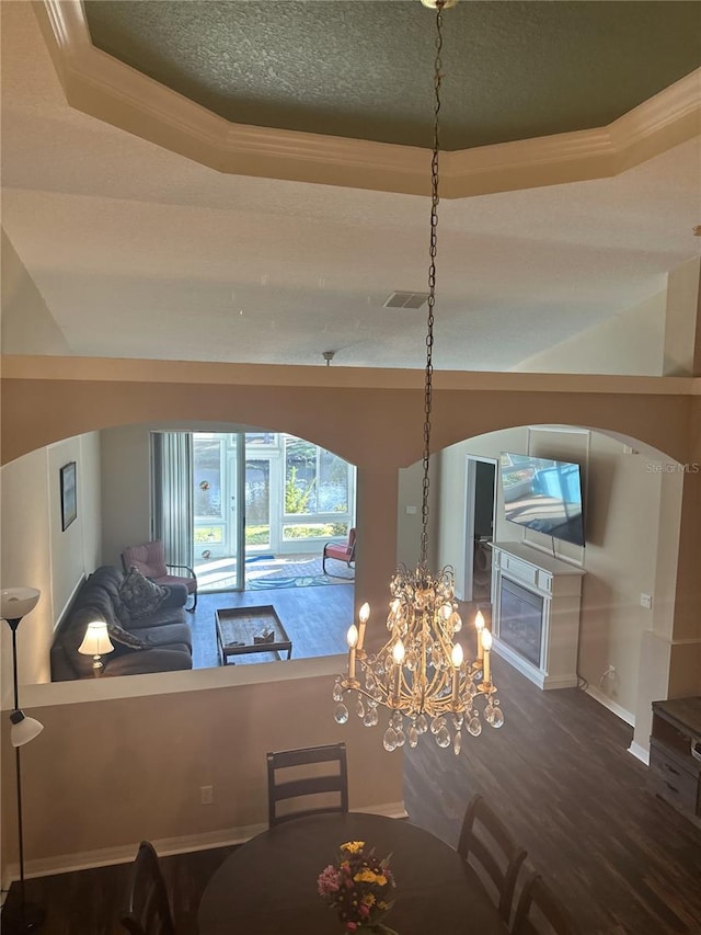 unfurnished dining area with a raised ceiling, crown molding, hardwood / wood-style flooring, and a textured ceiling