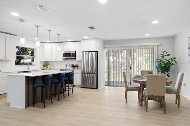 kitchen with white cabinets, light wood-type flooring, stainless steel appliances, and hanging light fixtures