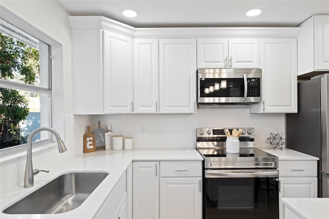 kitchen with white cabinetry, sink, stainless steel appliances, light stone counters, and backsplash