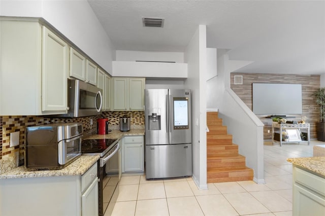 kitchen featuring decorative backsplash, light tile patterned floors, a textured ceiling, appliances with stainless steel finishes, and light stone counters