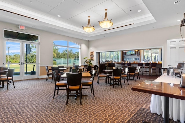 carpeted dining space with a raised ceiling, a wealth of natural light, and french doors