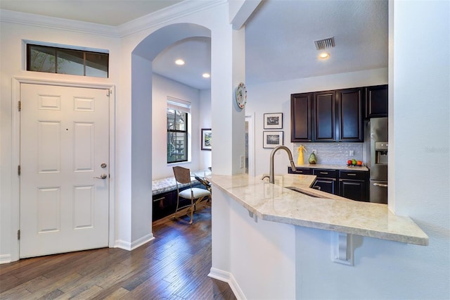 kitchen featuring dark wood-type flooring, a kitchen breakfast bar, sink, kitchen peninsula, and stainless steel fridge with ice dispenser