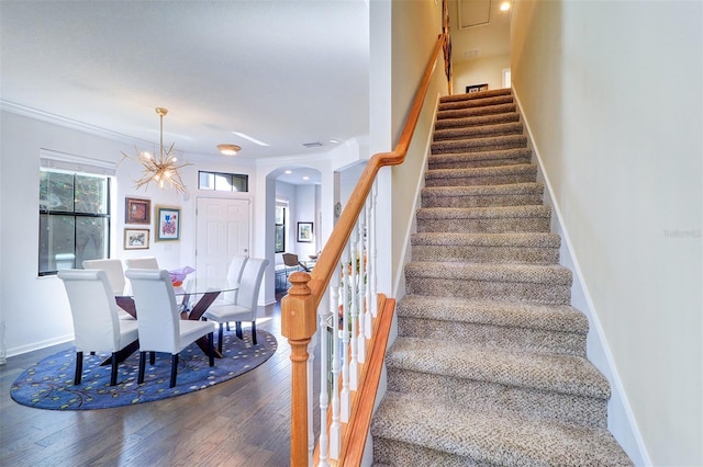 stairway featuring wood-type flooring, crown molding, and a notable chandelier