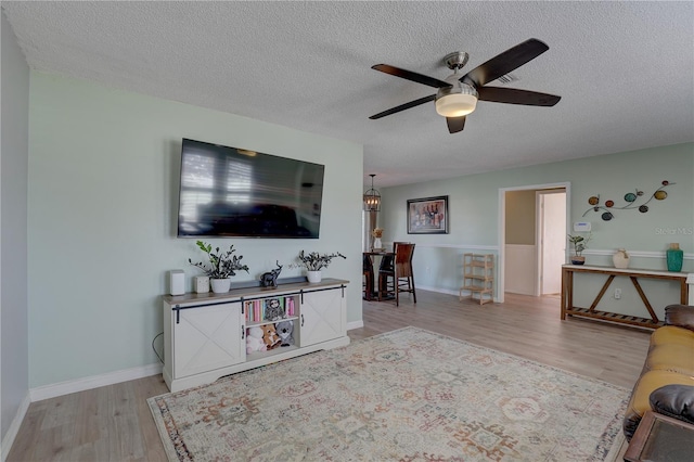 living room featuring ceiling fan, a textured ceiling, and light hardwood / wood-style flooring