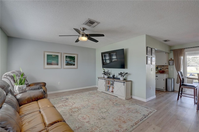 living room with ceiling fan, light hardwood / wood-style floors, and a textured ceiling