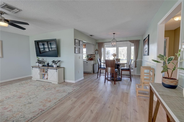 dining area with ceiling fan with notable chandelier, a textured ceiling, and light hardwood / wood-style floors