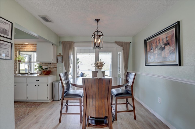 dining area with a textured ceiling, a healthy amount of sunlight, light wood-type flooring, and sink