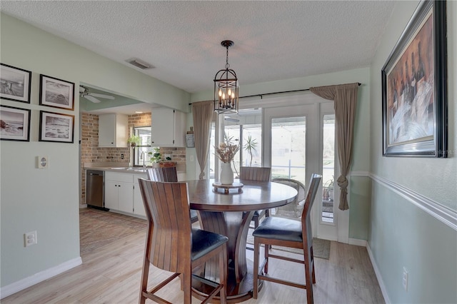 dining area with ceiling fan with notable chandelier, light hardwood / wood-style floors, and a textured ceiling