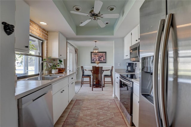 kitchen featuring appliances with stainless steel finishes, a tray ceiling, sink, pendant lighting, and white cabinetry