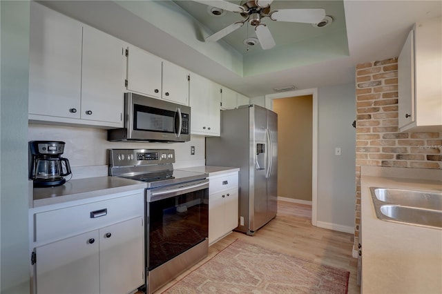 kitchen with appliances with stainless steel finishes, a raised ceiling, ceiling fan, light hardwood / wood-style flooring, and white cabinets