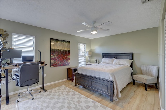 bedroom with a textured ceiling, light hardwood / wood-style floors, multiple windows, and ceiling fan