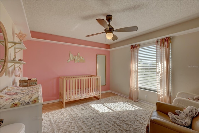 bedroom with ceiling fan, hardwood / wood-style floors, a nursery area, and a textured ceiling