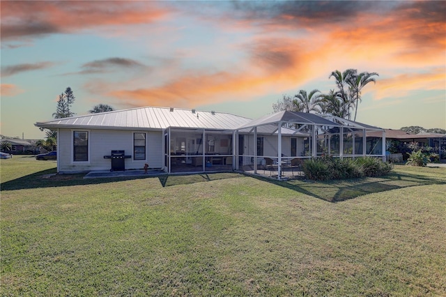 back house at dusk with glass enclosure, a patio area, and a yard