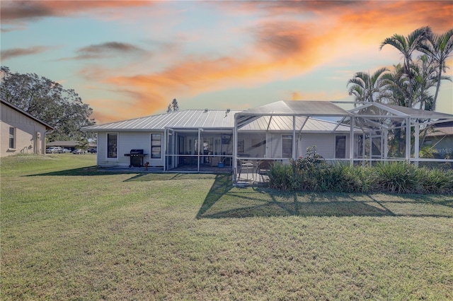 back house at dusk featuring a lanai and a lawn