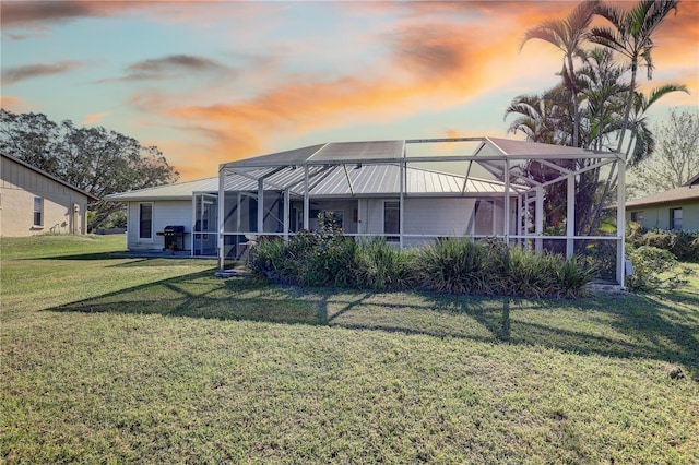 back house at dusk with glass enclosure and a yard