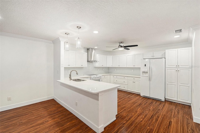 kitchen with sink, hanging light fixtures, wall chimney exhaust hood, white fridge with ice dispenser, and white cabinetry