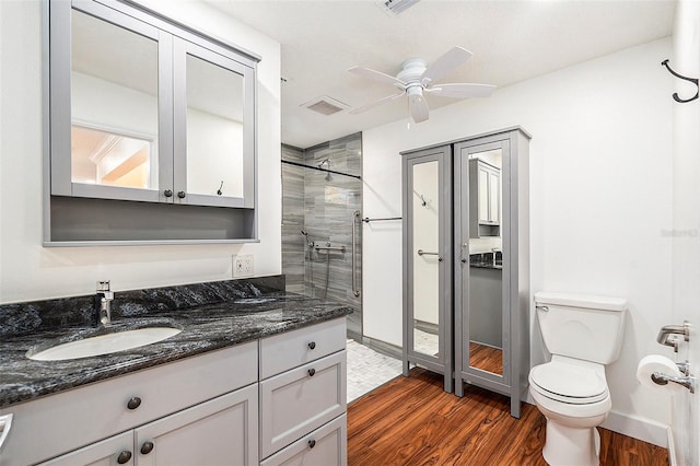 bathroom featuring vanity, ceiling fan, toilet, tiled shower, and wood-type flooring