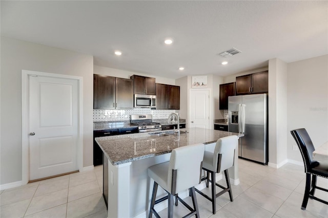 kitchen featuring a center island with sink, a kitchen breakfast bar, sink, appliances with stainless steel finishes, and dark brown cabinets