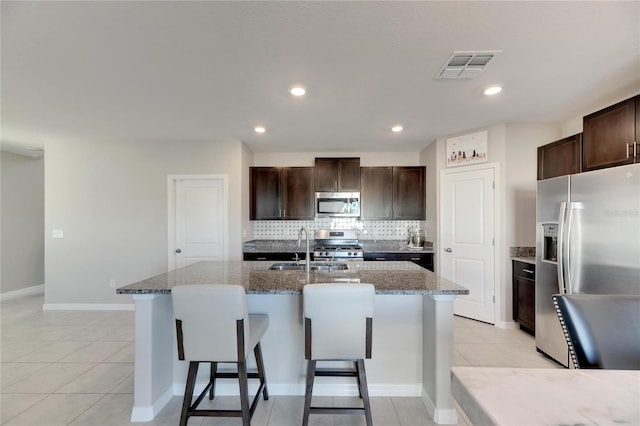 kitchen featuring light stone countertops, backsplash, stainless steel appliances, a kitchen island with sink, and sink