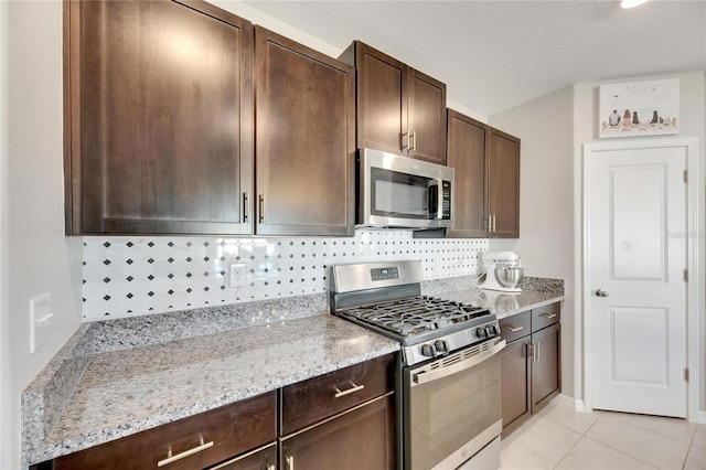 kitchen with decorative backsplash, light stone countertops, light tile patterned floors, appliances with stainless steel finishes, and dark brown cabinets