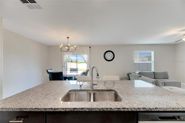 kitchen featuring a center island with sink, sink, hanging light fixtures, stainless steel dishwasher, and light stone counters