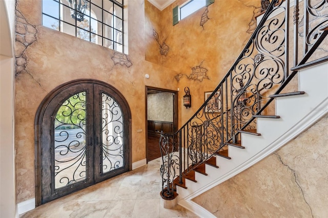 entryway with ornamental molding, a high ceiling, and french doors