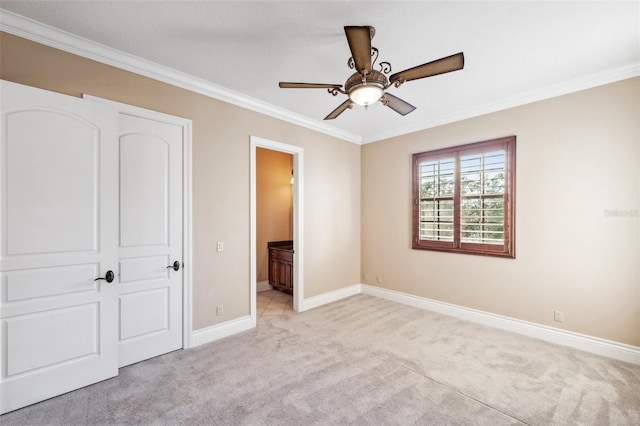 unfurnished bedroom featuring ceiling fan, ensuite bathroom, light colored carpet, and ornamental molding