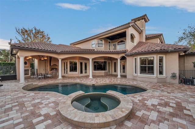 rear view of property with a swimming pool with hot tub, a patio, and a balcony