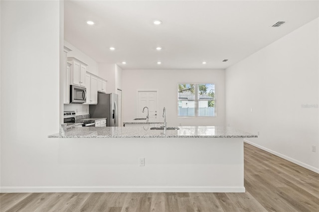 kitchen featuring light hardwood / wood-style flooring, light stone countertops, white cabinetry, kitchen peninsula, and stainless steel appliances