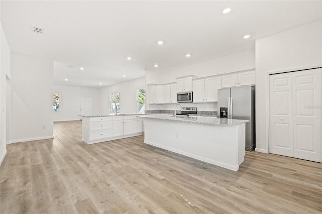 kitchen featuring a center island with sink, light wood-type flooring, light stone counters, white cabinetry, and stainless steel appliances