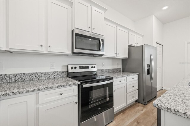 kitchen with light stone counters, light hardwood / wood-style flooring, white cabinets, and appliances with stainless steel finishes