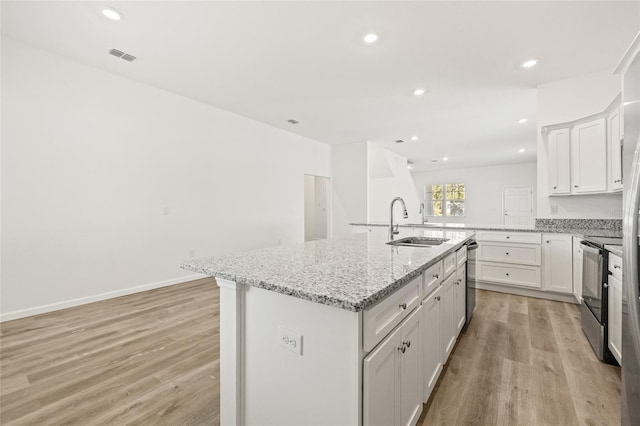 kitchen featuring light stone countertops, a kitchen island with sink, sink, light hardwood / wood-style flooring, and stainless steel electric range