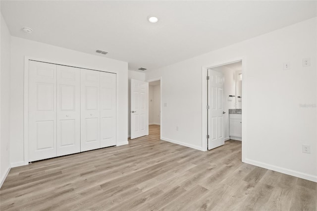 unfurnished bedroom with ensuite bath, a closet, and light wood-type flooring