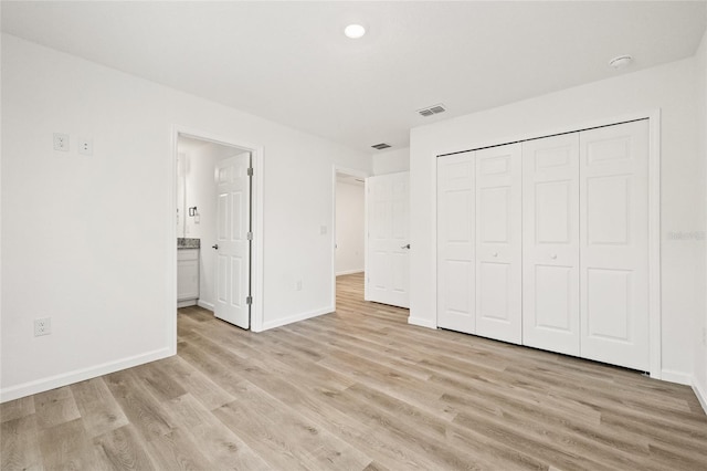 unfurnished bedroom featuring light hardwood / wood-style floors, a closet, and ensuite bath