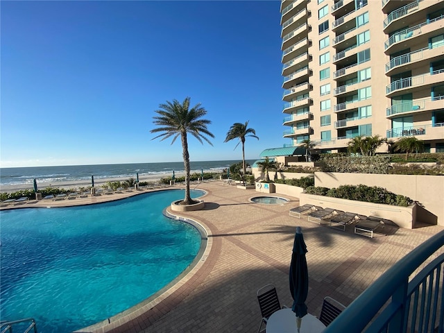 view of pool featuring a water view, a patio, and a hot tub