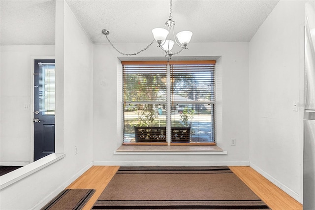 unfurnished dining area featuring a textured ceiling, hardwood / wood-style flooring, and a notable chandelier