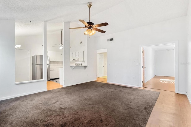 unfurnished living room with light carpet, high vaulted ceiling, a textured ceiling, and ceiling fan