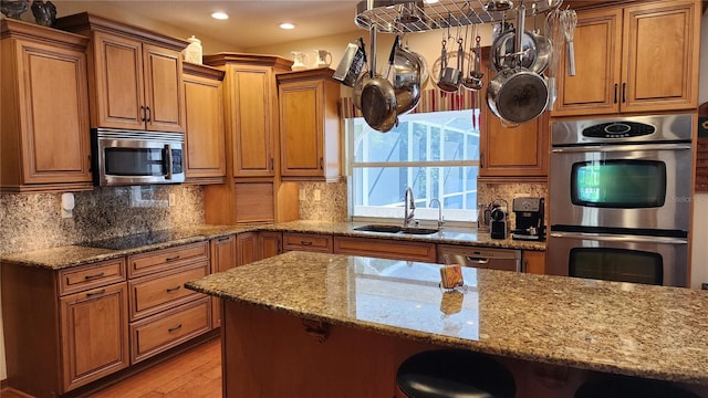 kitchen with sink, light stone counters, light hardwood / wood-style floors, a kitchen bar, and appliances with stainless steel finishes