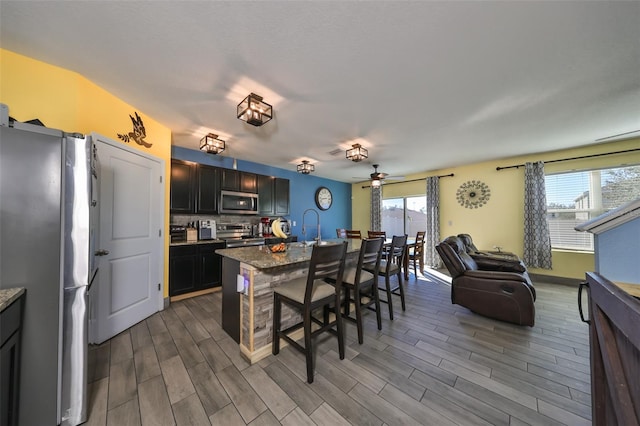 kitchen featuring a kitchen breakfast bar, dark stone counters, stainless steel appliances, ceiling fan, and dark wood-type flooring