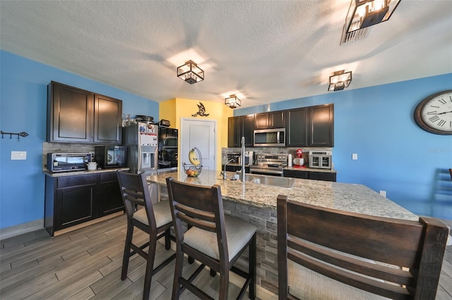 kitchen with hardwood / wood-style floors, sink, a textured ceiling, an island with sink, and stainless steel appliances