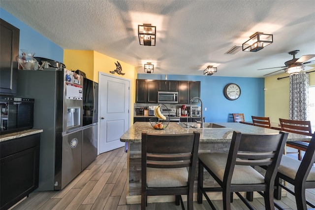 kitchen with sink, light hardwood / wood-style flooring, a kitchen bar, a kitchen island with sink, and appliances with stainless steel finishes