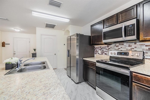 kitchen with sink, decorative backsplash, a textured ceiling, dark brown cabinets, and stainless steel appliances