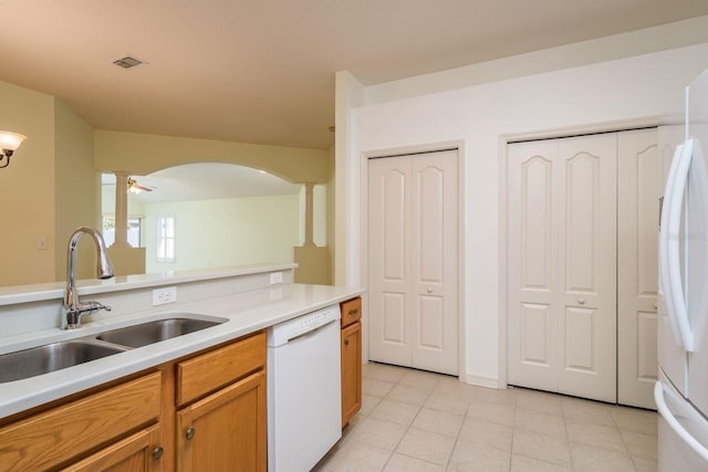 kitchen with white appliances, light tile patterned floors, arched walkways, a sink, and light countertops