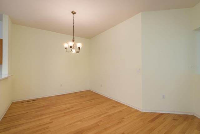 spare room featuring a notable chandelier, light wood-type flooring, and baseboards