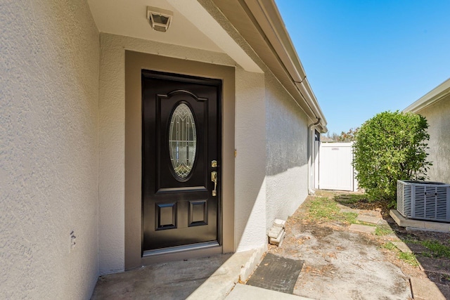 doorway to property with central AC unit, stucco siding, and fence