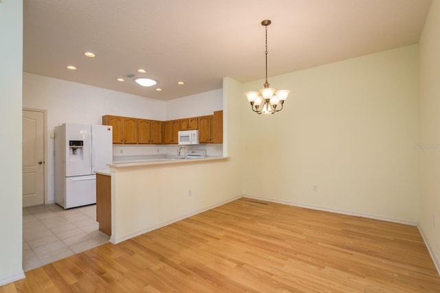 kitchen with white appliances, light wood finished floors, a peninsula, brown cabinets, and a chandelier