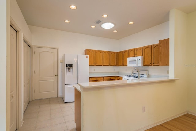 kitchen with white appliances, a peninsula, recessed lighting, light countertops, and brown cabinets